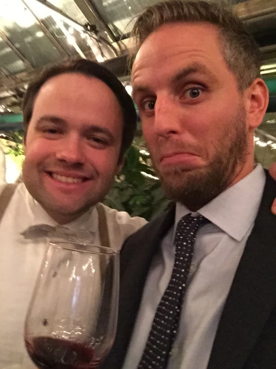 two men wearing neck ties posing with a wine glass