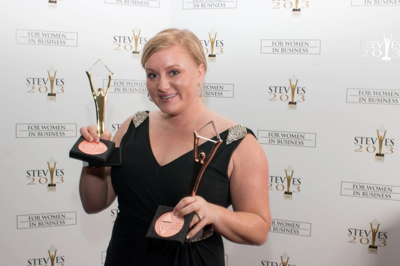 a woman is holding up several award cups