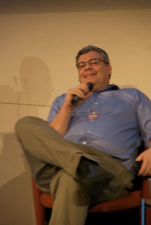 a man with glasses sitting down on a chair and speaking into a microphone