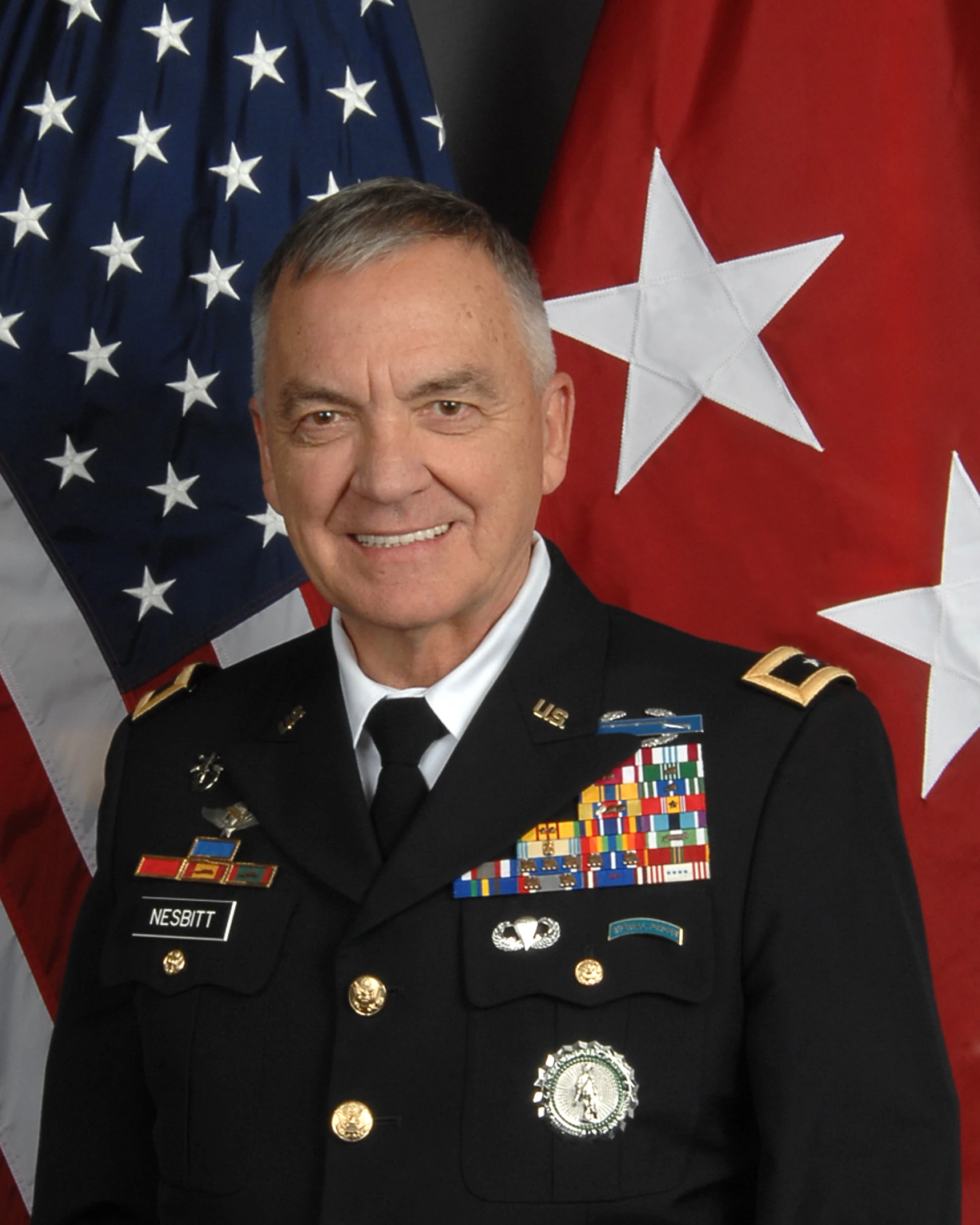 an older gentleman in uniform smiles with two american flags behind him