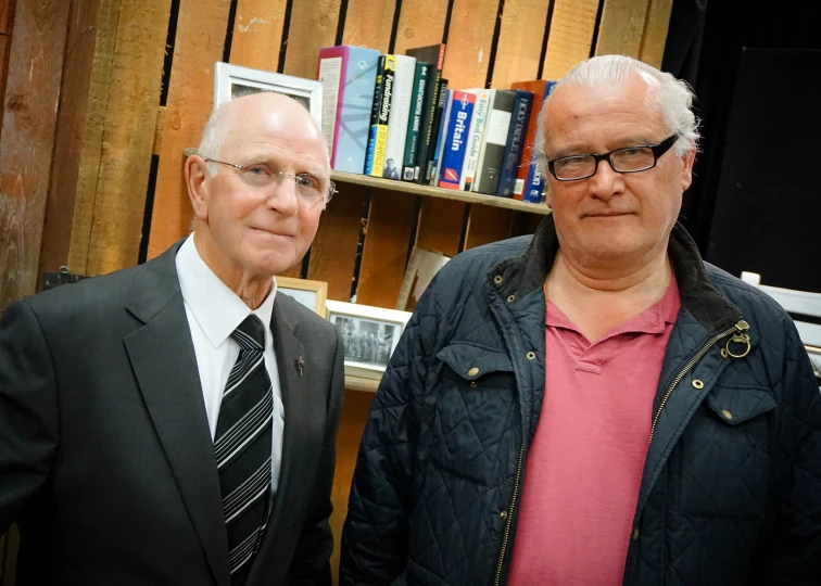 two men standing in front of a bookshelf