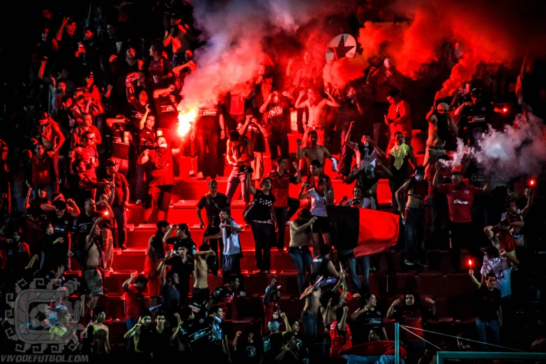 a bunch of people are standing and watching as the crowd holds up red smoke