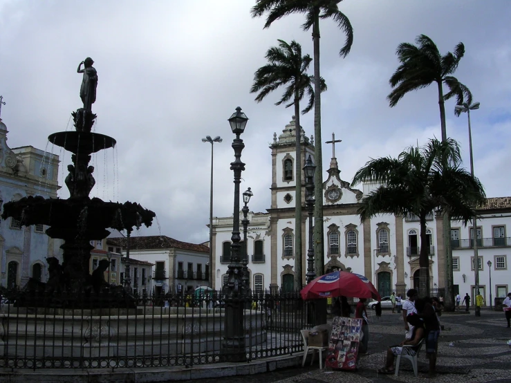 a park with benches next to a fountain with many palm trees