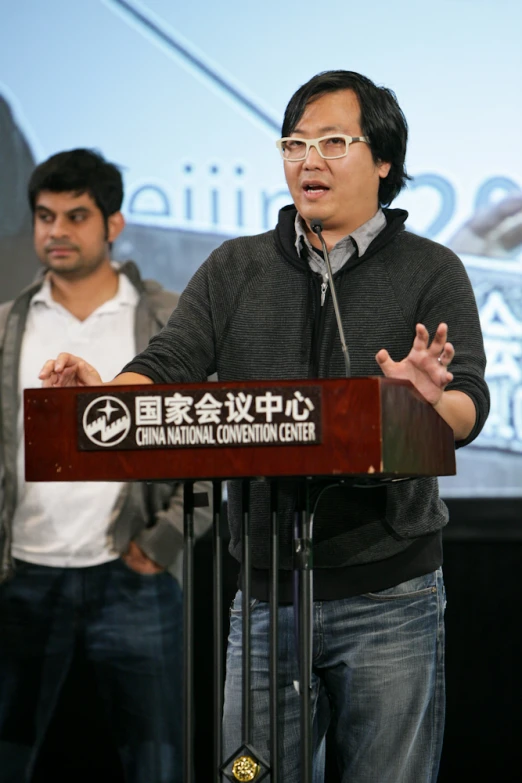 an asian american man is speaking at a microphone