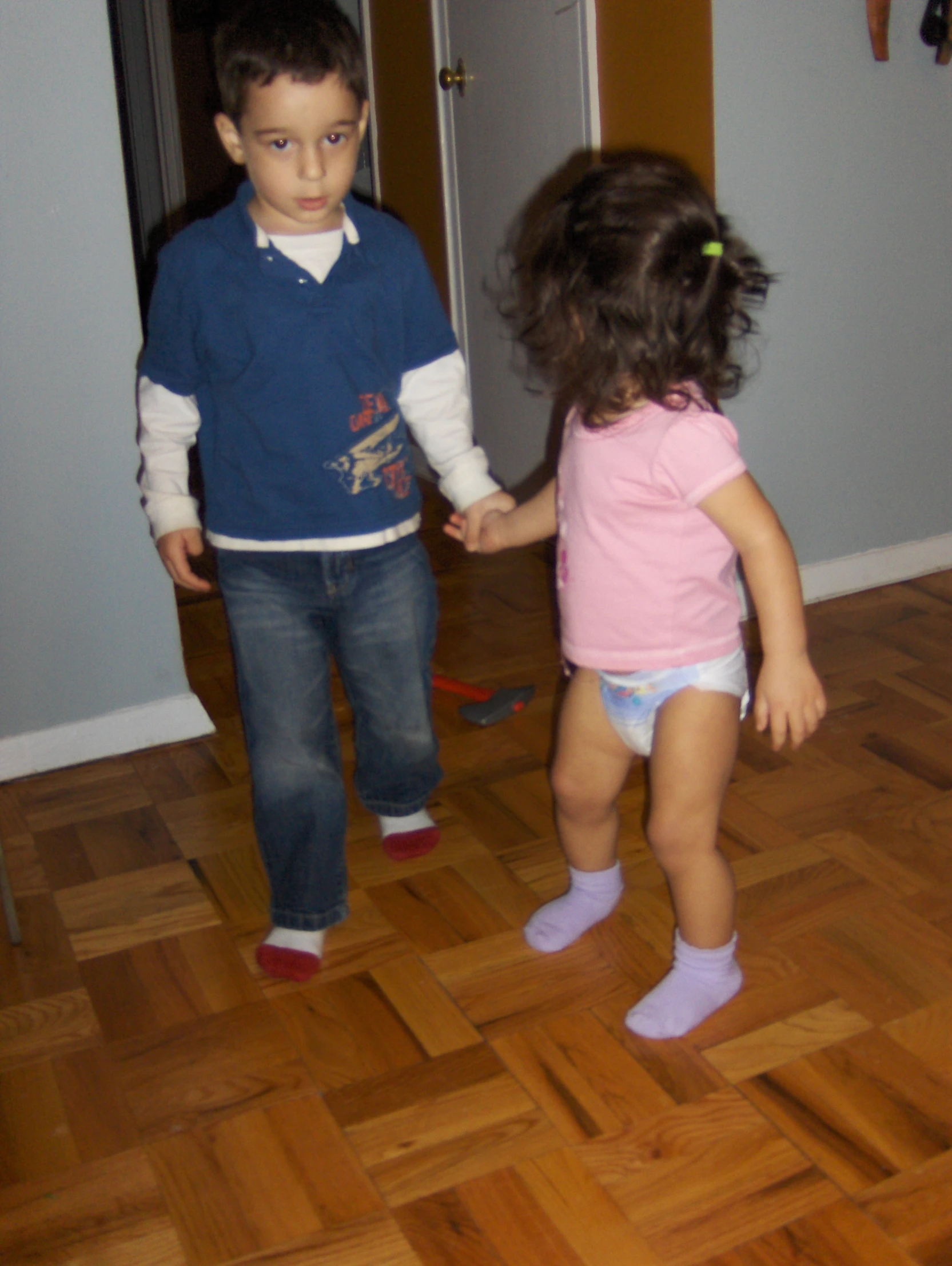 two children are standing in the hallway one has their hand on the other's leg