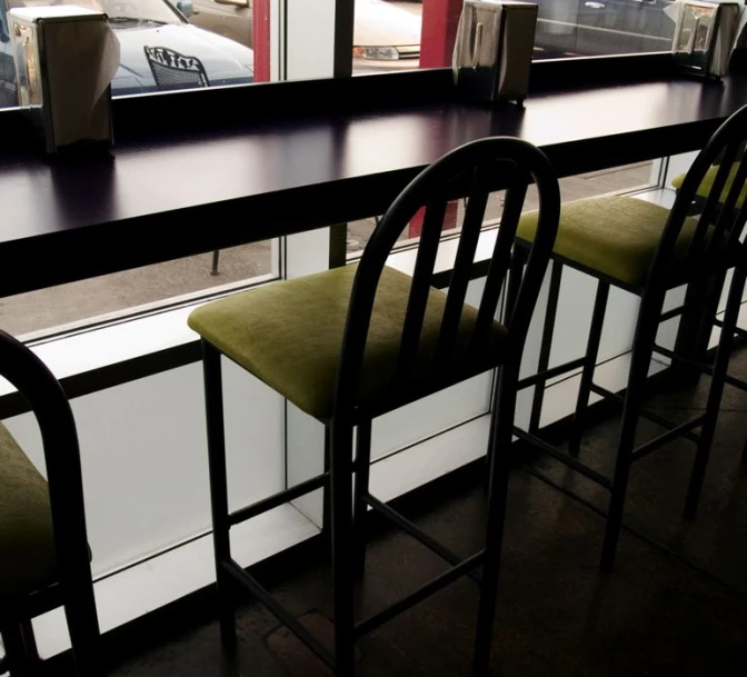 bar with two black chairs and three green seats and one black chair and the window behind them