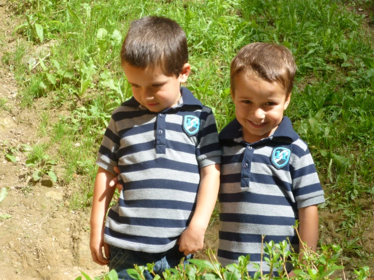 two boys are standing in the dirt and some grass