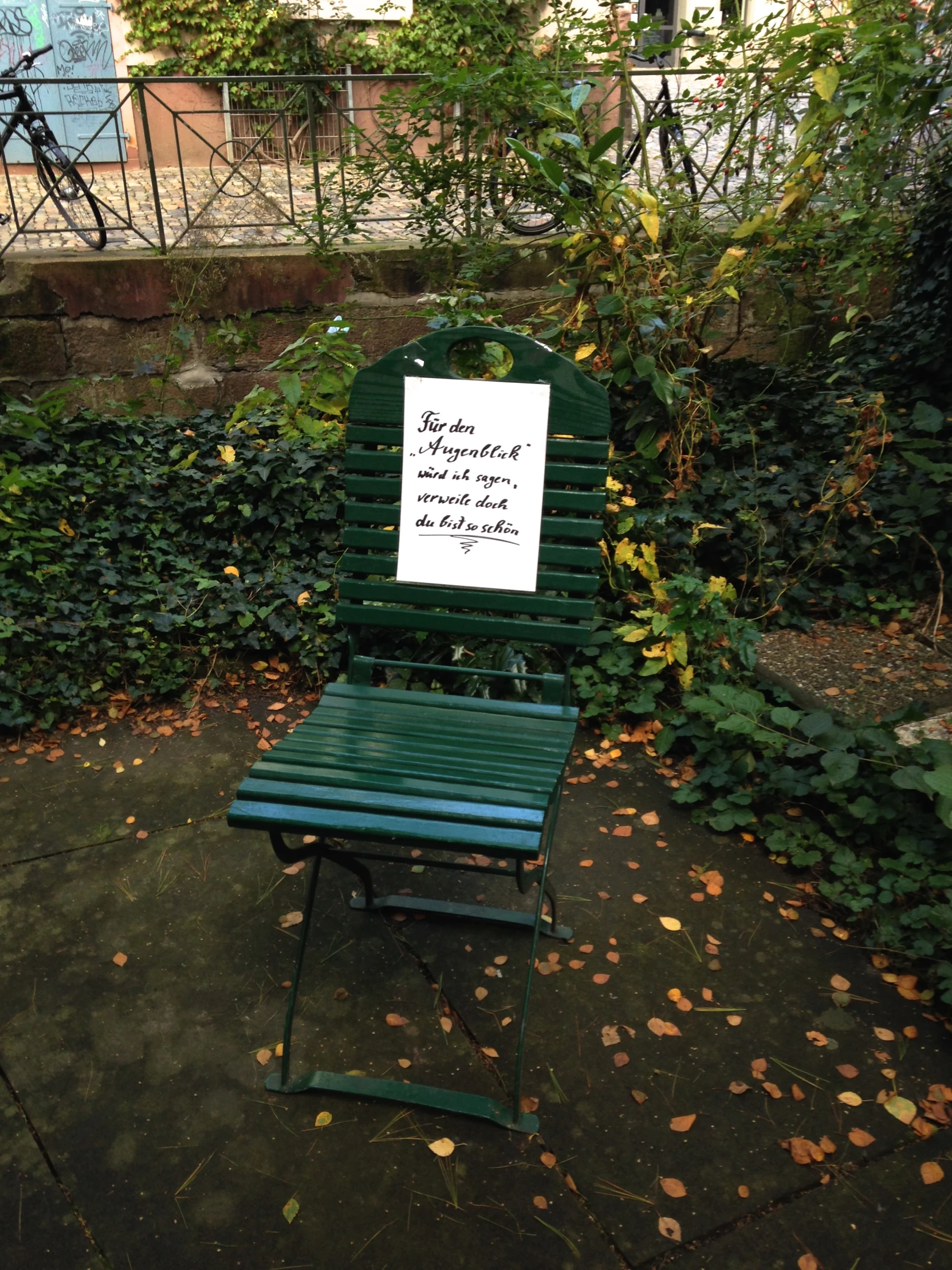 a sign is attached to a wooden bench in front of trees