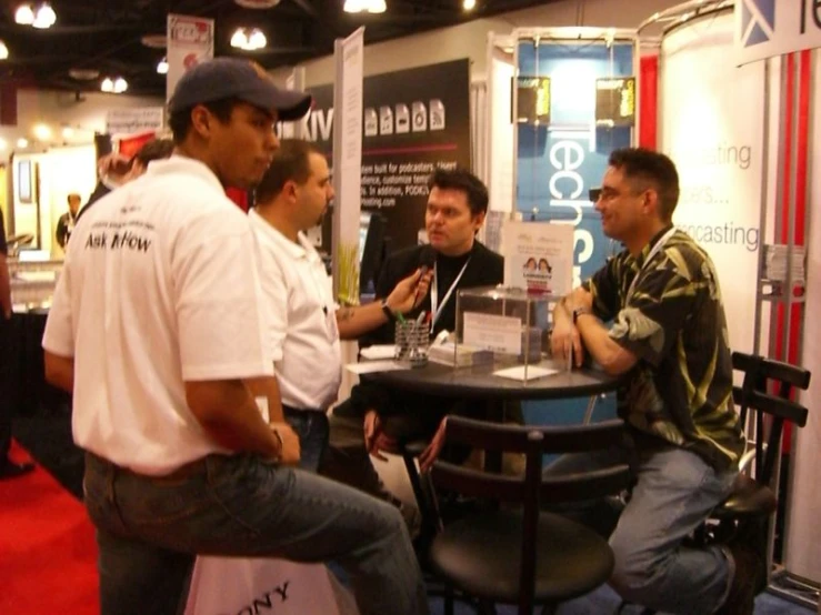 a man speaking to a group of men in front of a trade show booth