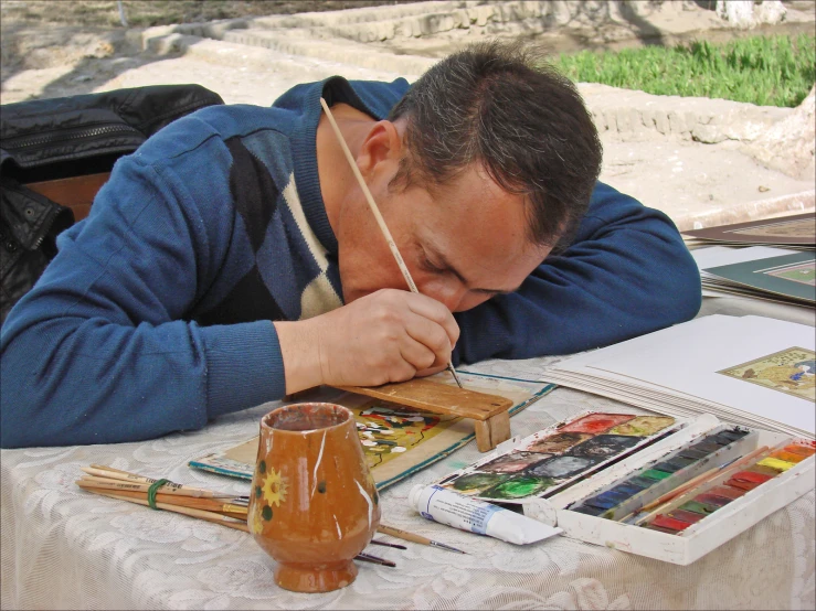 man lying his head down on table with art supplies