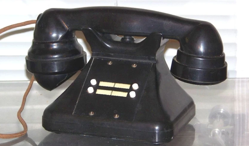 an old black rotary phone sitting on a glass table