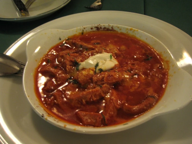 a bowl of meat and tomato soup on a white plate