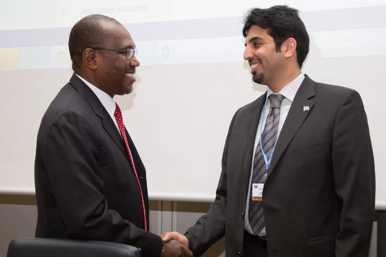 two men shaking hands in front of a projection screen