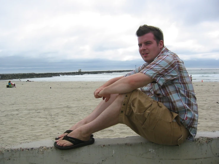 a man sitting on top of a cement wall next to a beach