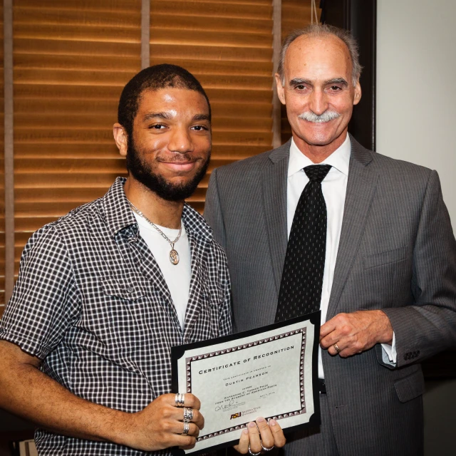 a smiling man is holding an award next to another gentleman