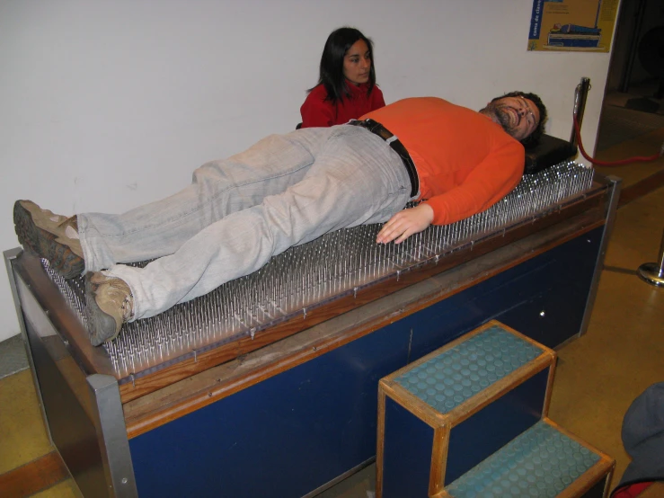 a man lays on top of a bed while another sits nearby