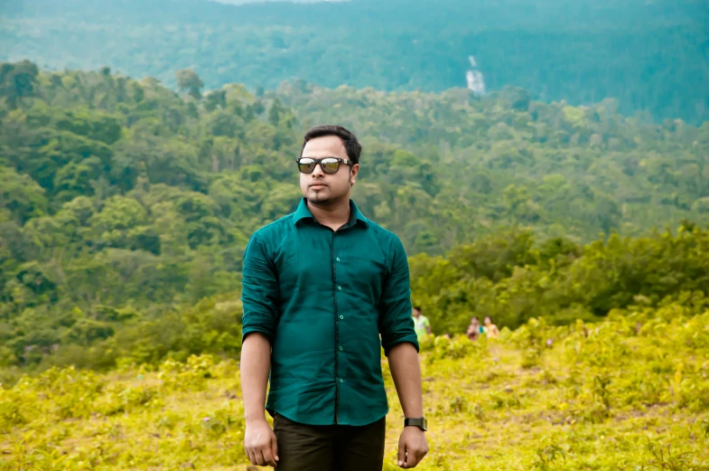 a man wearing sunglasses standing in front of a green forest