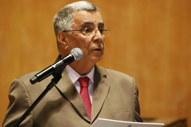 a person wearing glasses stands in front of a microphone and looks to his left