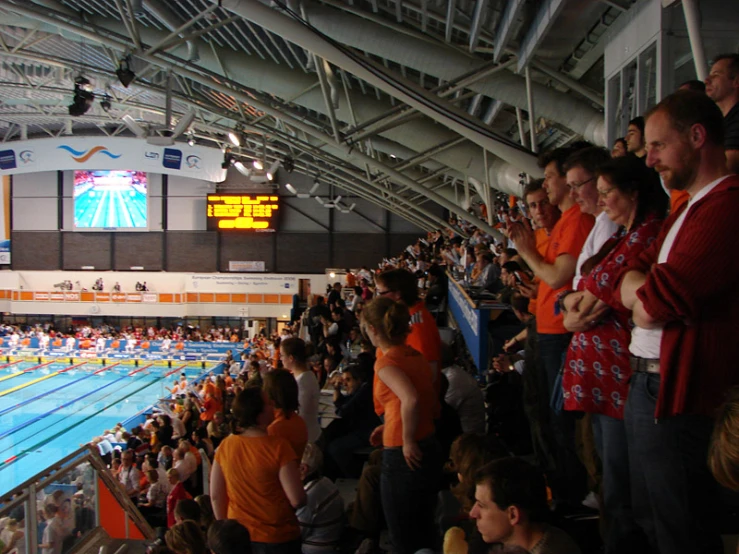 a crowd of people sitting at the side of a pool watching a man swim