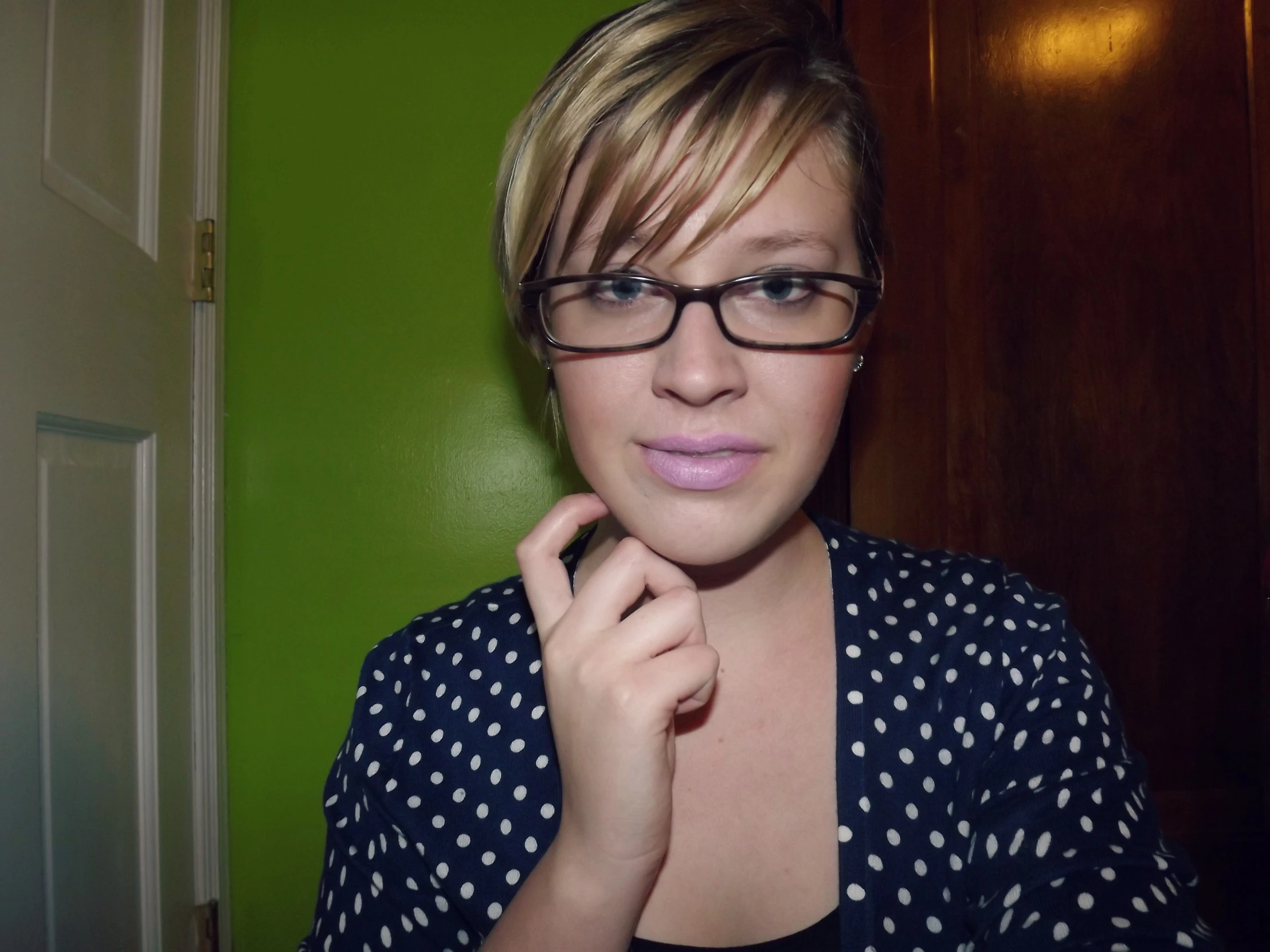 a young woman wearing glasses standing by the green wall