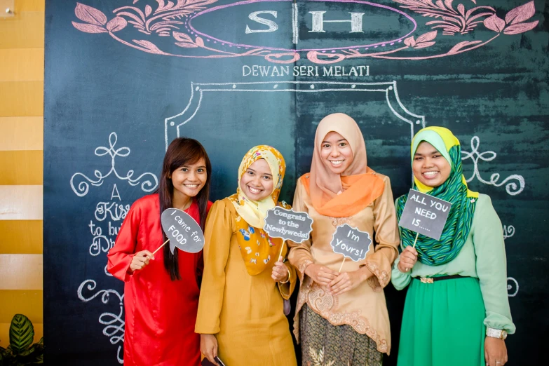 three women smiling while holding signs reading sh