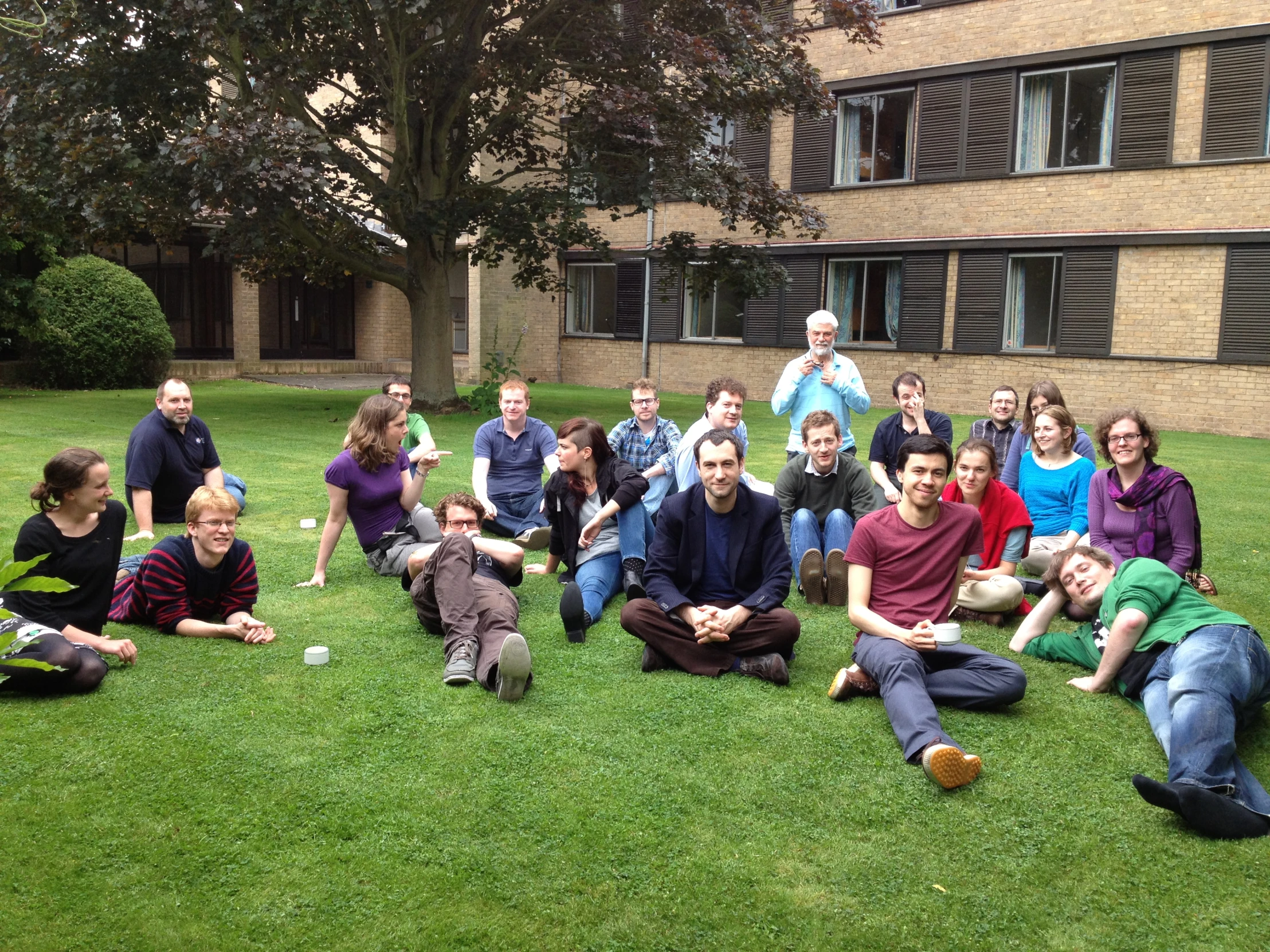 people sitting on the grass posing for a po with one man throwing a ball