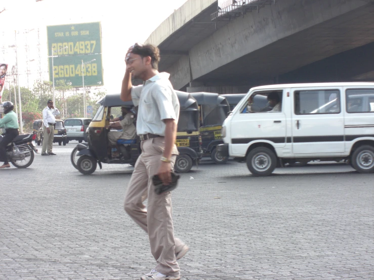 a man walking across a street talking on a cell phone