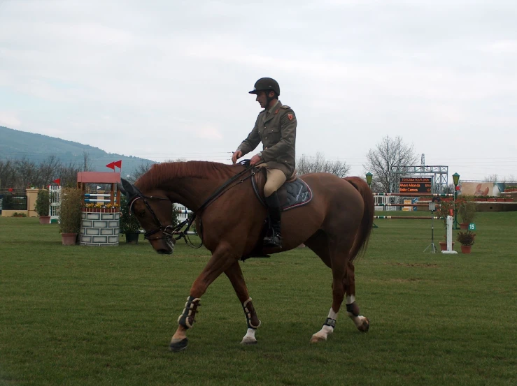 a woman wearing a uniform riding a brown horse in the field