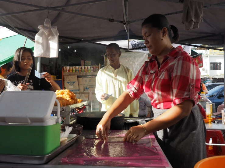 three women are outside preparing food under an umbrella