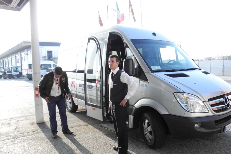 two men stand beside a silver van and each has its doors open