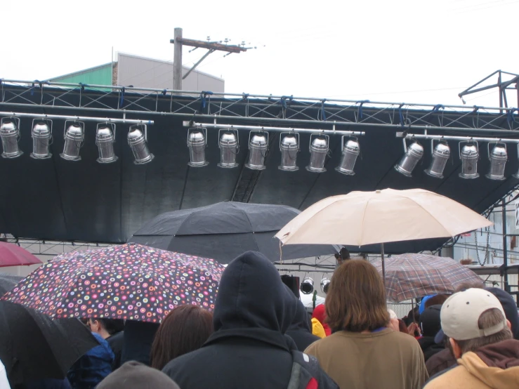 several people standing under umbrellas next to a stage