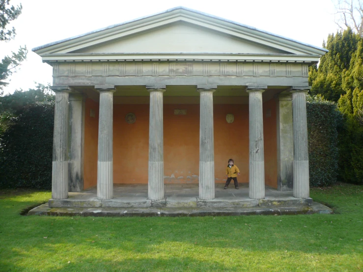 a man walking in front of pillars in a grassy field