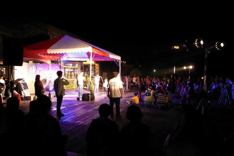 people stand at an outdoor concert under a tent at night