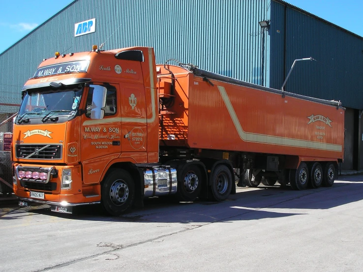 an orange semi truck outside a building with other vehicles