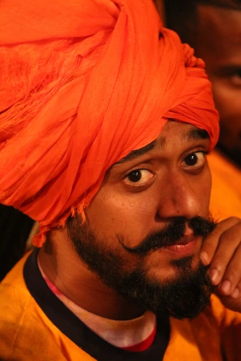 the man is wearing an orange turban and looking to his left