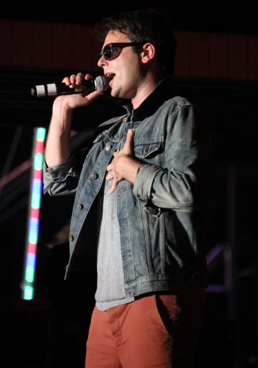 a man standing in front of a microphone wearing sunglasses