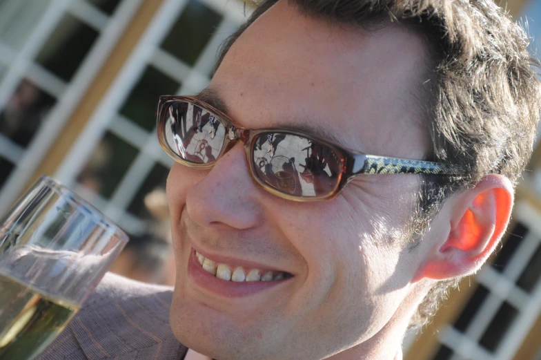 a smiling man with glasses holds up a wine glass