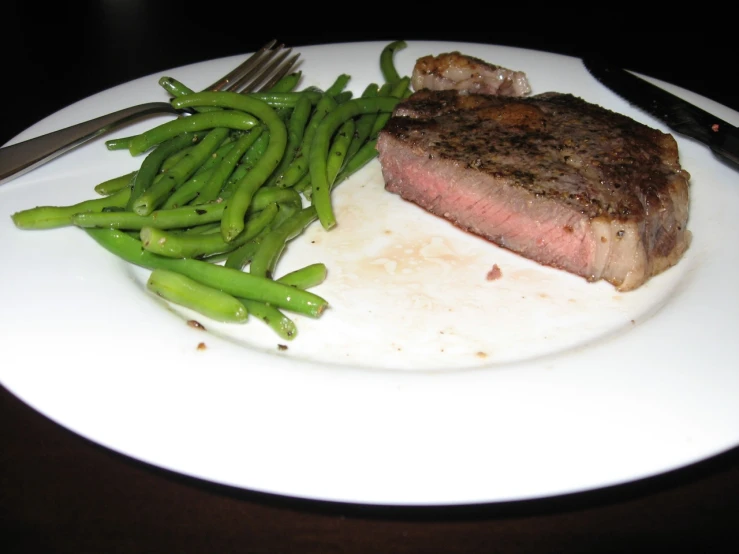 a piece of steak and some green beans on a white plate