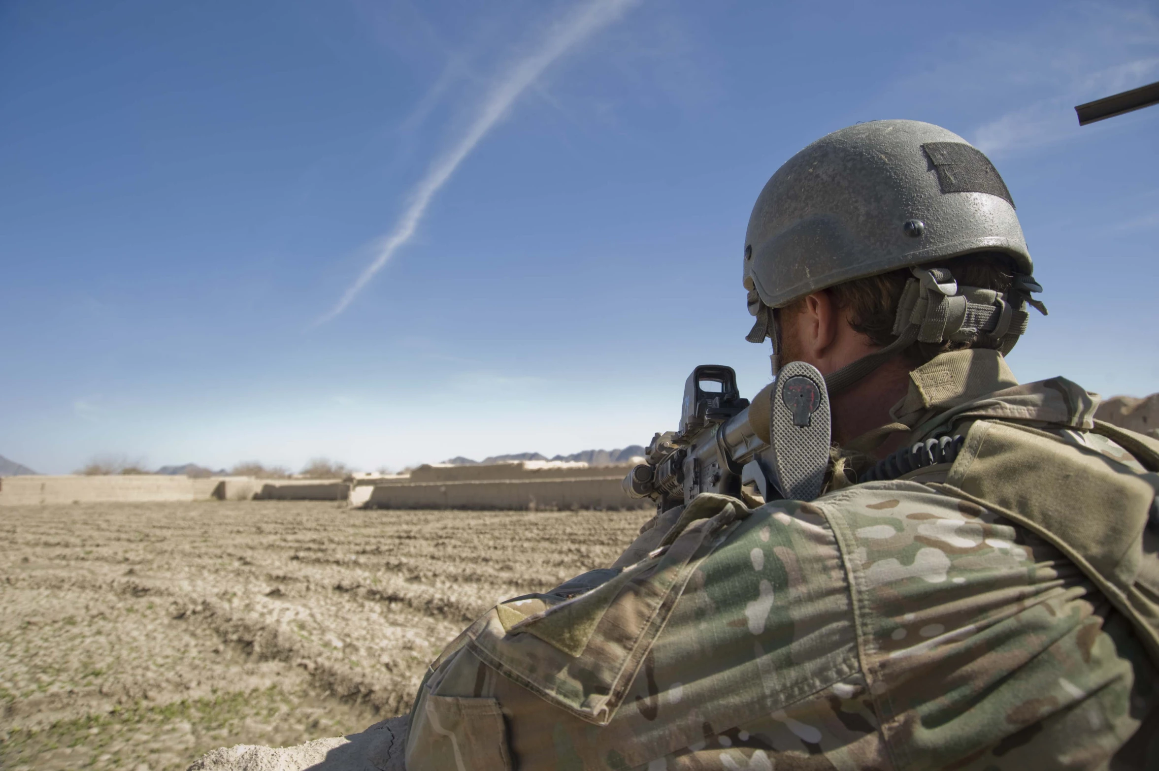 a man in camouflage holds a gun while wearing head gear