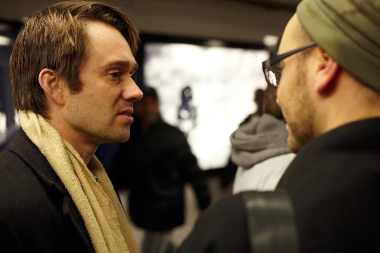 a man talks to another man wearing a scarf