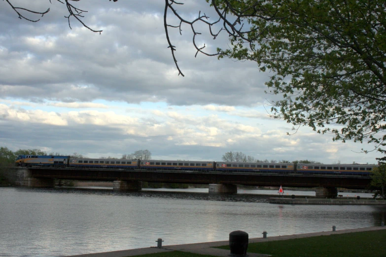 an electric train crosses over a river with trees in the foreground