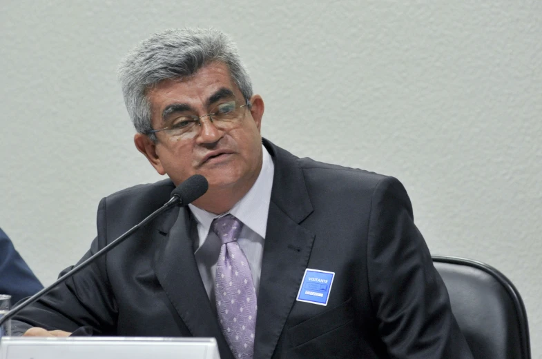 a man in business suit sitting in front of microphone at a table