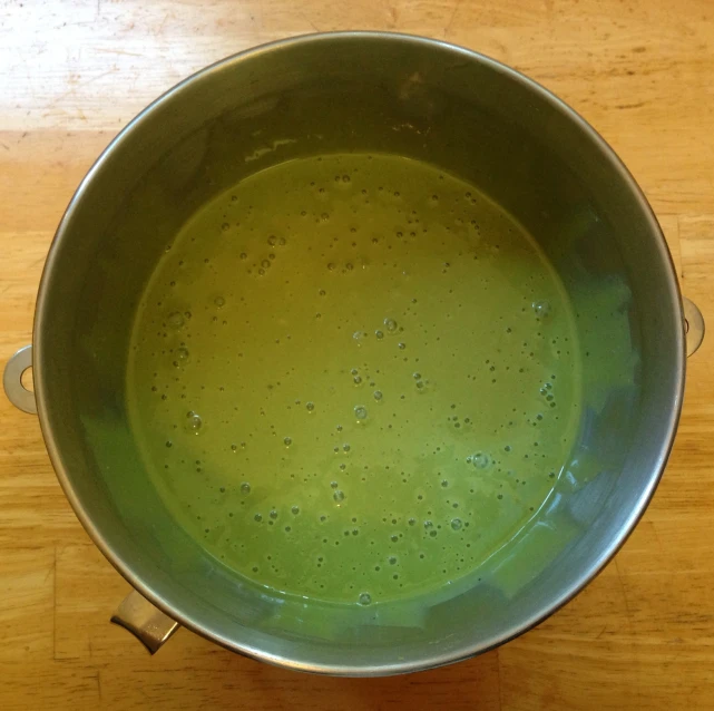 a green liquid in a silver pot on top of a wooden table