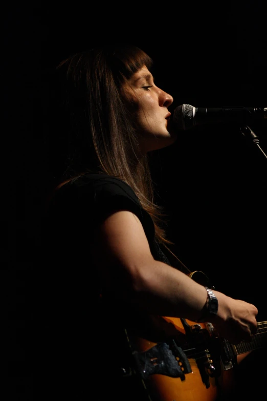 the woman is playing the guitar and singing into the microphone