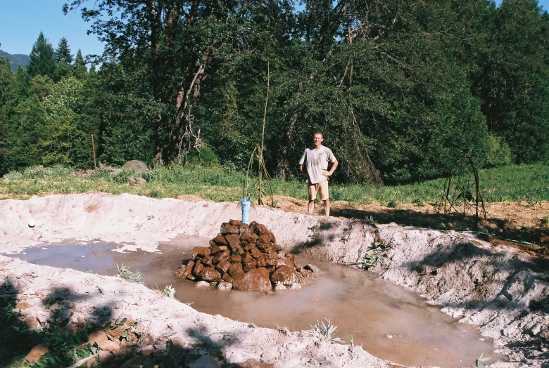 a man standing near a forest with lots of logs