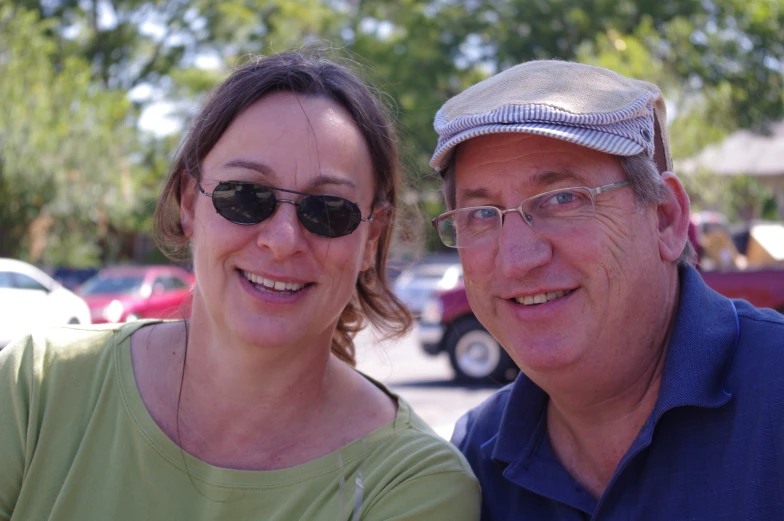 a man and woman pose together in front of parked cars