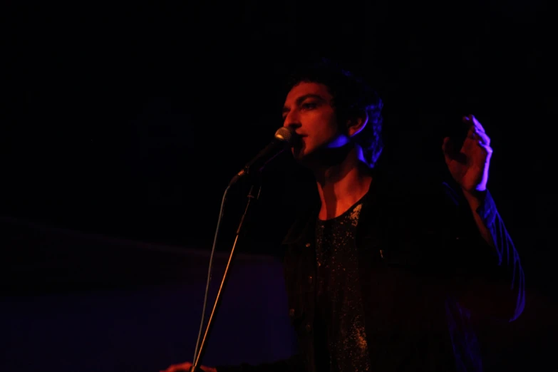 a woman in a black top stands at a microphone and looks to the side