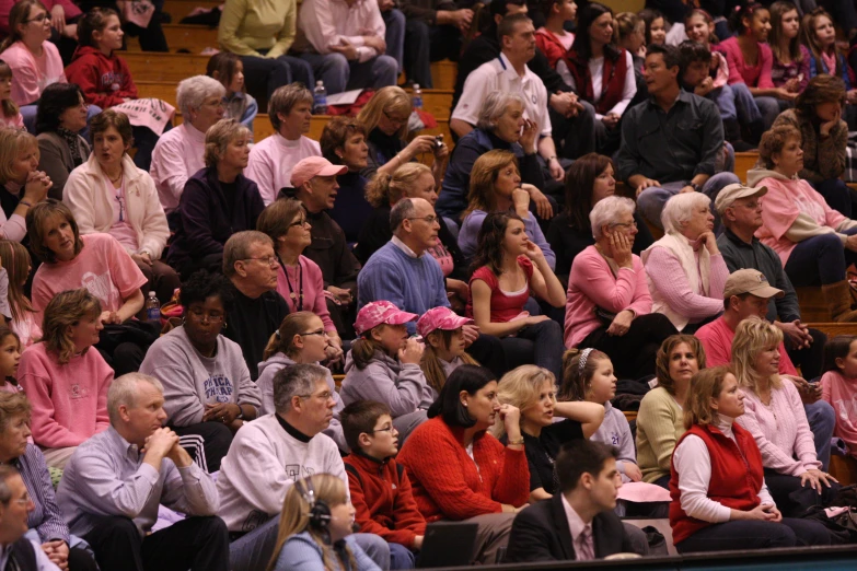 many people are sitting in the bleachers with pink hats