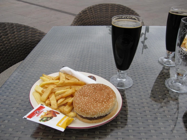 a hamburger and fries sit on a plate with drinks