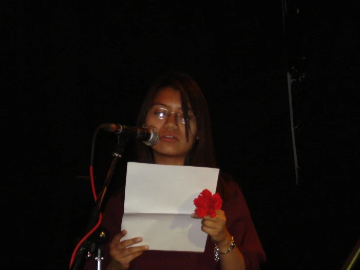 a woman in a red top and glasses holds a piece of paper with a flower on it